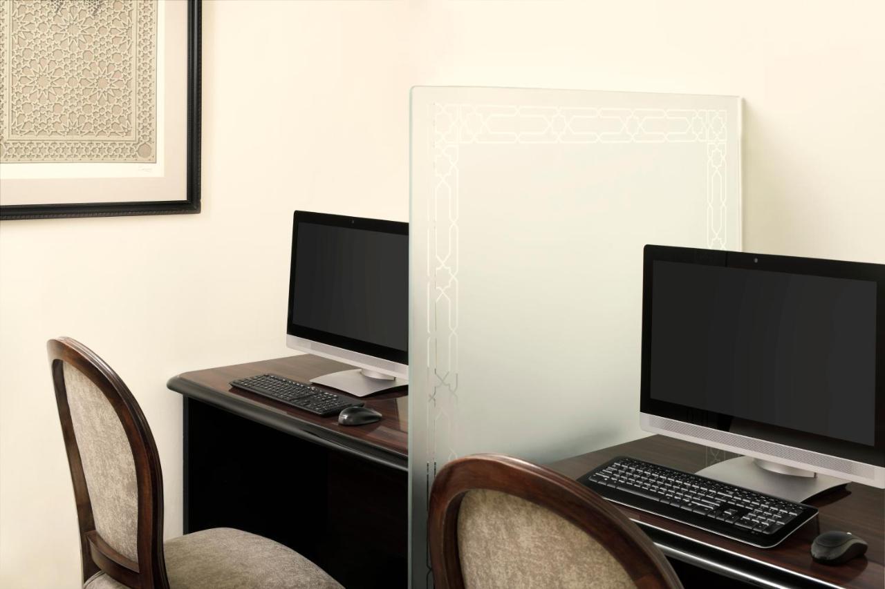 Intercontinental Dar Al Iman Madinah By Ihg Medina Exterior foto The photo shows a workspace featuring two computers set up on a dark wooden desk. Each computer has a monitor and a keyboard. A frosted glass partition is placed between the two workstations, providing some privacy. In the background, there is a fram