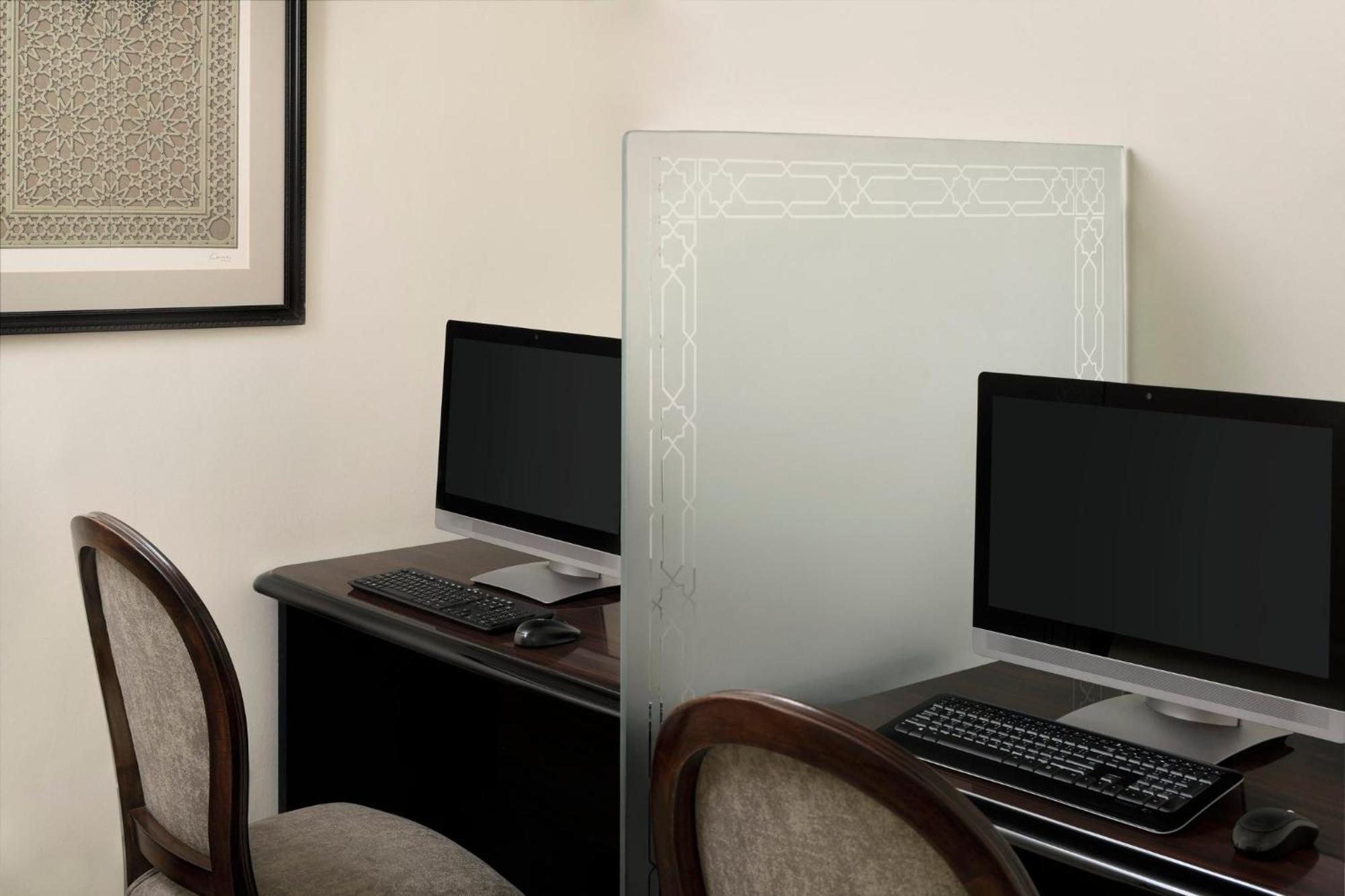 Intercontinental Dar Al Iman Madinah By Ihg Medina Exterior foto The photo shows a small office or workspace area featuring two computer stations. Each station has a black monitor, a keyboard, and appears to be set up on a dark wooden desk. A translucent glass partition is placed between the two workstations, prov