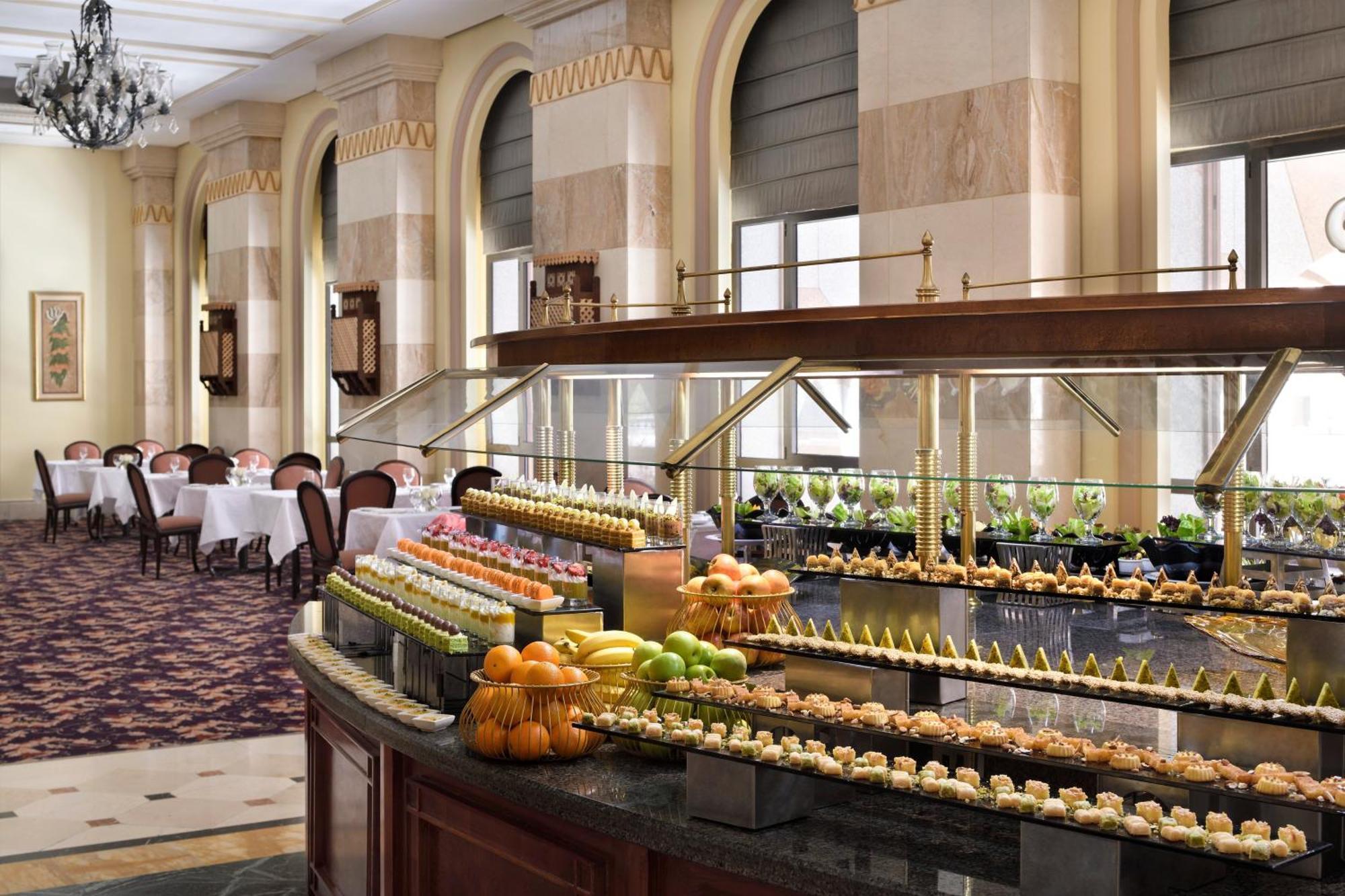 Intercontinental Dar Al Iman Madinah By Ihg Medina Exterior foto The photo depicts an elegant dining area featuring a buffet-style display. In the foreground, a beautifully arranged buffet counter showcases an array of desserts, including miniature pastries and colorful fruit. The setting has a sophisticated ambia