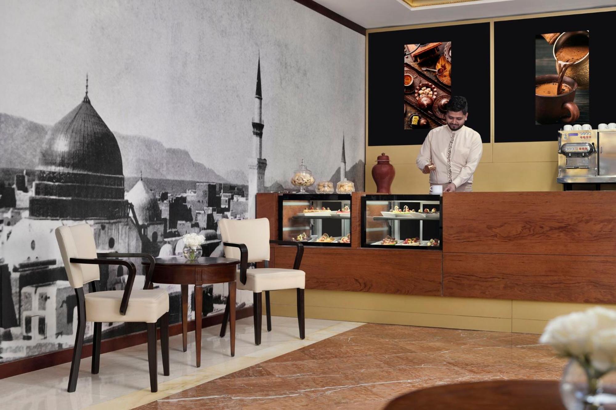 Intercontinental Dar Al Iman Madinah By Ihg Medina Exterior foto The photo shows a stylish interior of a café or pastry shop. In the background, there is a large black-and-white mural depicting a cityscape, featuring a prominent dome and minaret, suggesting an architectural style that could be from a Middle Easter
