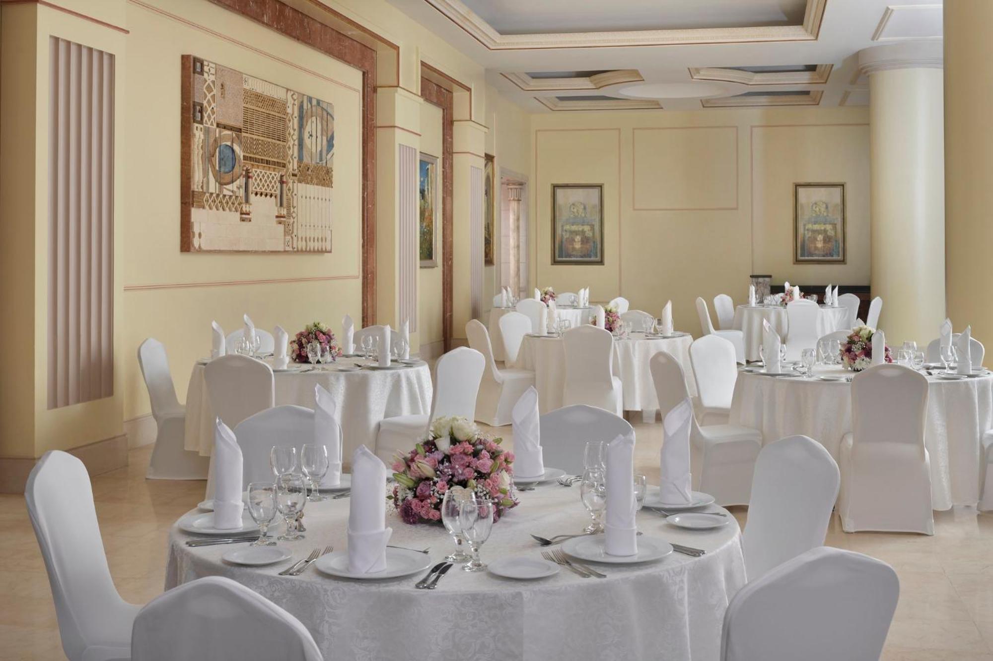 Intercontinental Dar Al Iman Madinah By Ihg Medina Exterior foto The photo shows an elegantly arranged dining or function room. There are round tables covered with white tablecloths, each set with fine dining ware including glassware, utensils, and neatly folded white napkins. Some tables have floral centerpieces 