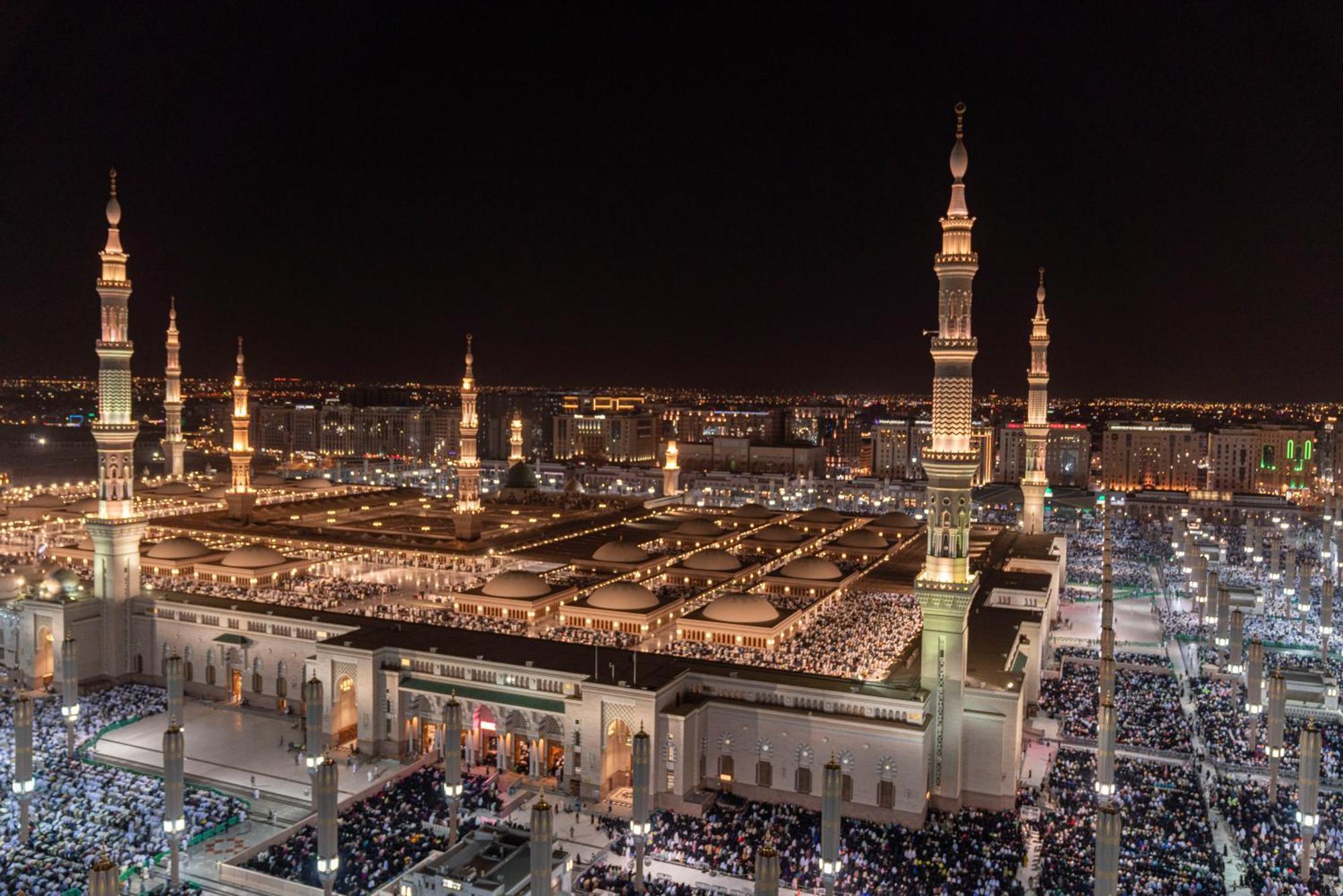 Intercontinental Dar Al Iman Madinah By Ihg Medina Exterior foto The photo shows a panoramic view of a large mosque complex illuminated at night. It features tall minarets with lights, a vast courtyard filled with people, and a beautifully lit architectural design. The overall ambiance suggests a significant space