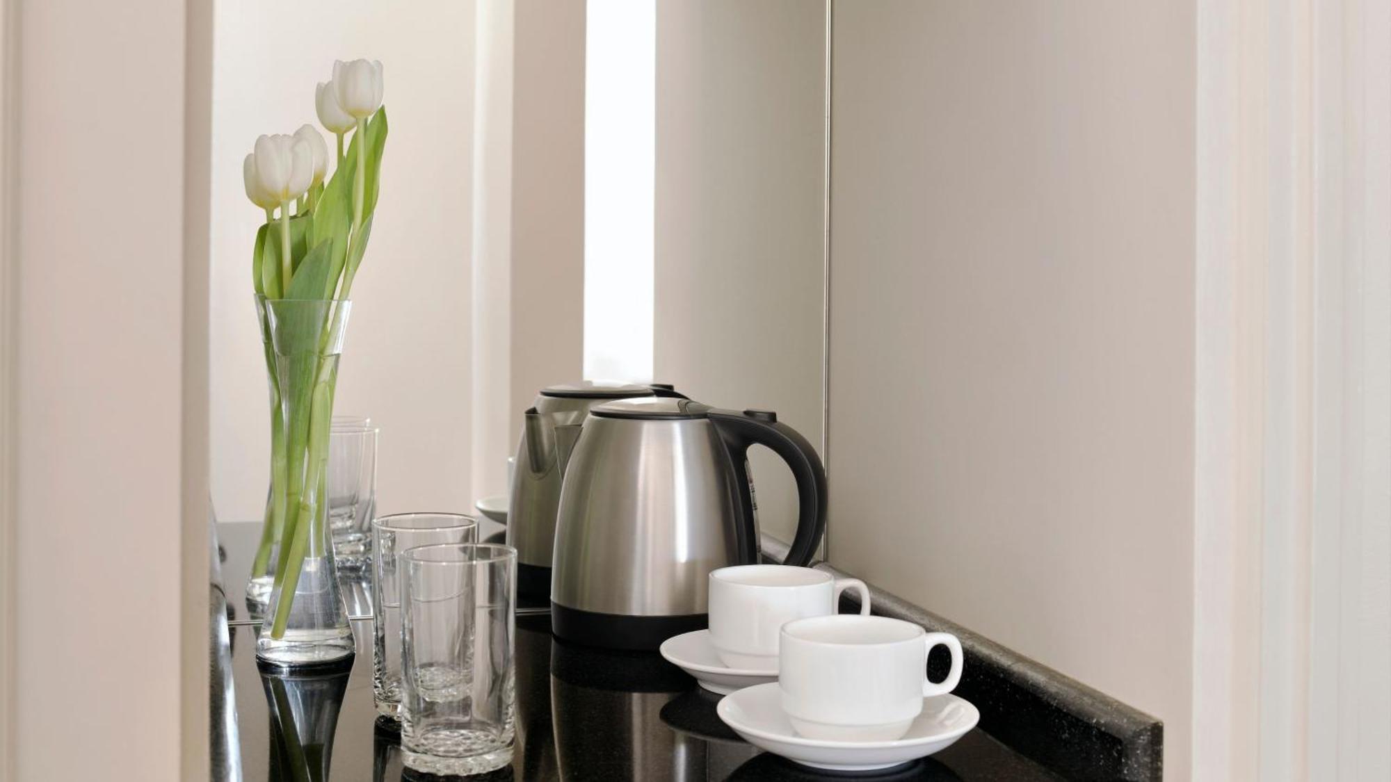 Intercontinental Dar Al Iman Madinah By Ihg Medina Exterior foto The photo depicts a neatly arranged beverage area. In the foreground, there are two white coffee cups on small saucers. Next to them, there are two clear drinking glasses. In the background, there is a silver electric kettle, which is positioned next