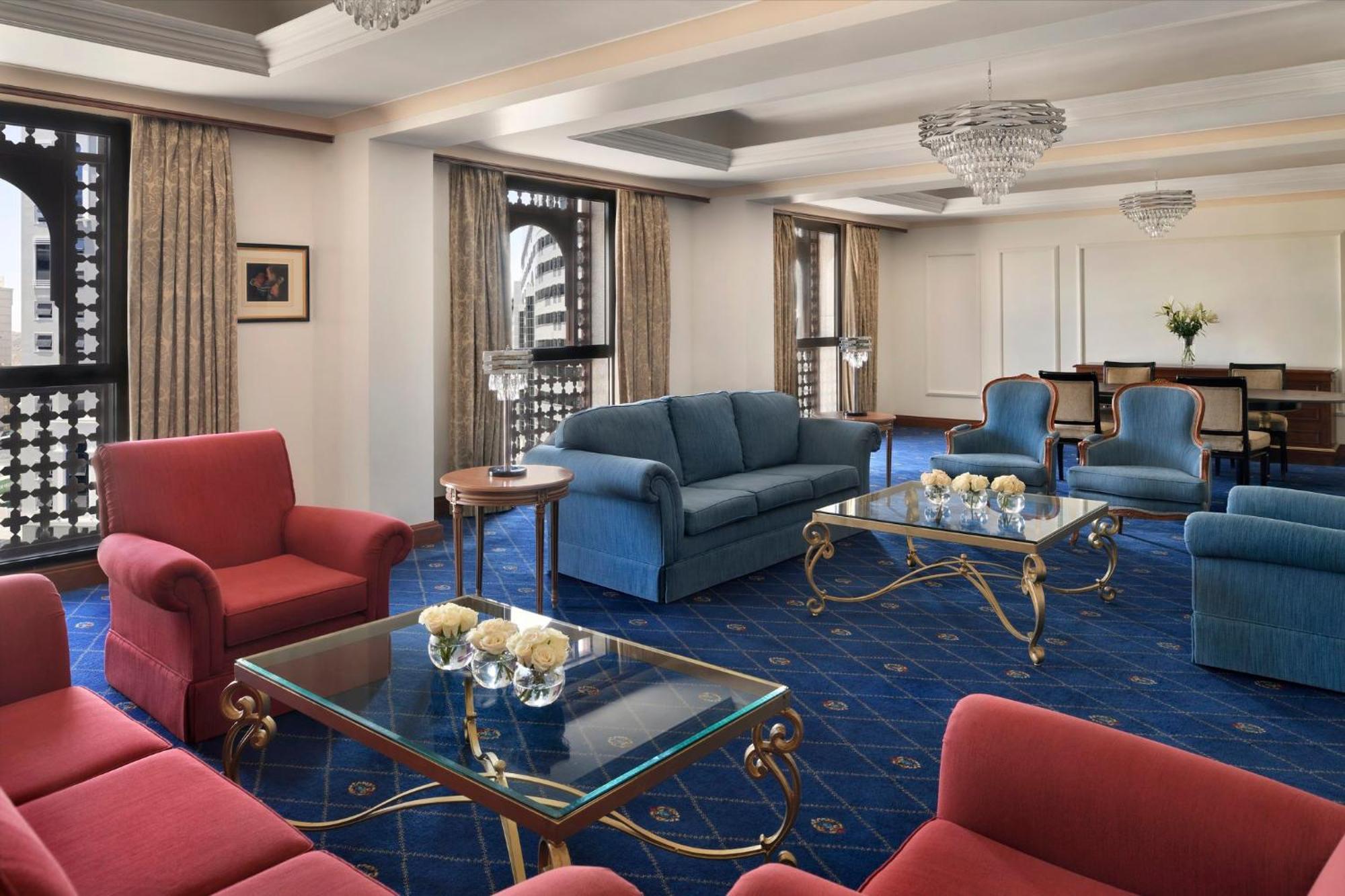 Intercontinental Dar Al Iman Madinah By Ihg Medina Exterior foto The photo shows a luxurious living space or lounge area. It features a combination of furniture, including a blue sofa, several red armchairs, and glass-top coffee tables with gold accents. The flooring is carpeted in a deep blue, and the walls are a