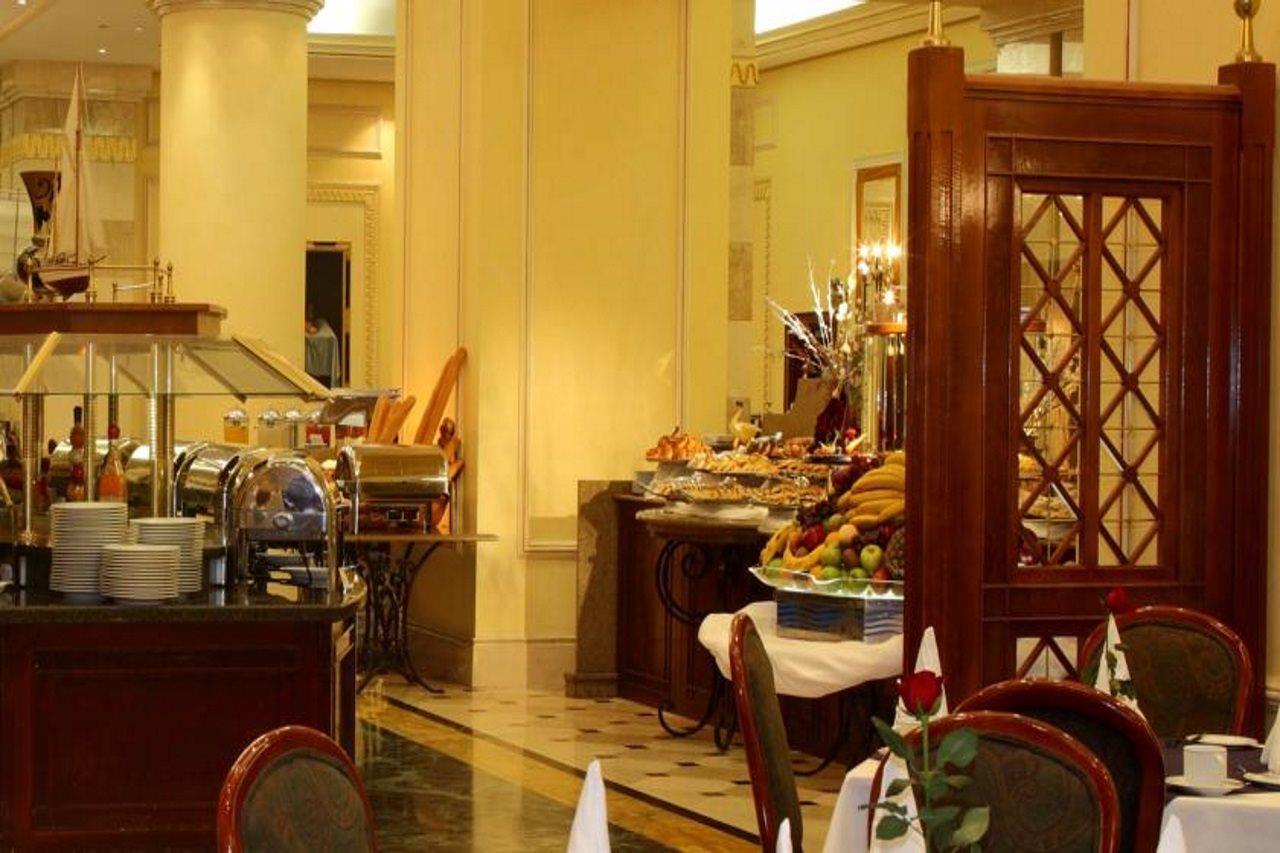 Intercontinental Dar Al Iman Madinah By Ihg Medina Exterior foto The photo shows an elegant dining area, likely within a restaurant or a hotel. There's a buffet setup on one side with various food items displayed, including pastries and fruits. The room features warm lighting, polished floors, and decorative walls