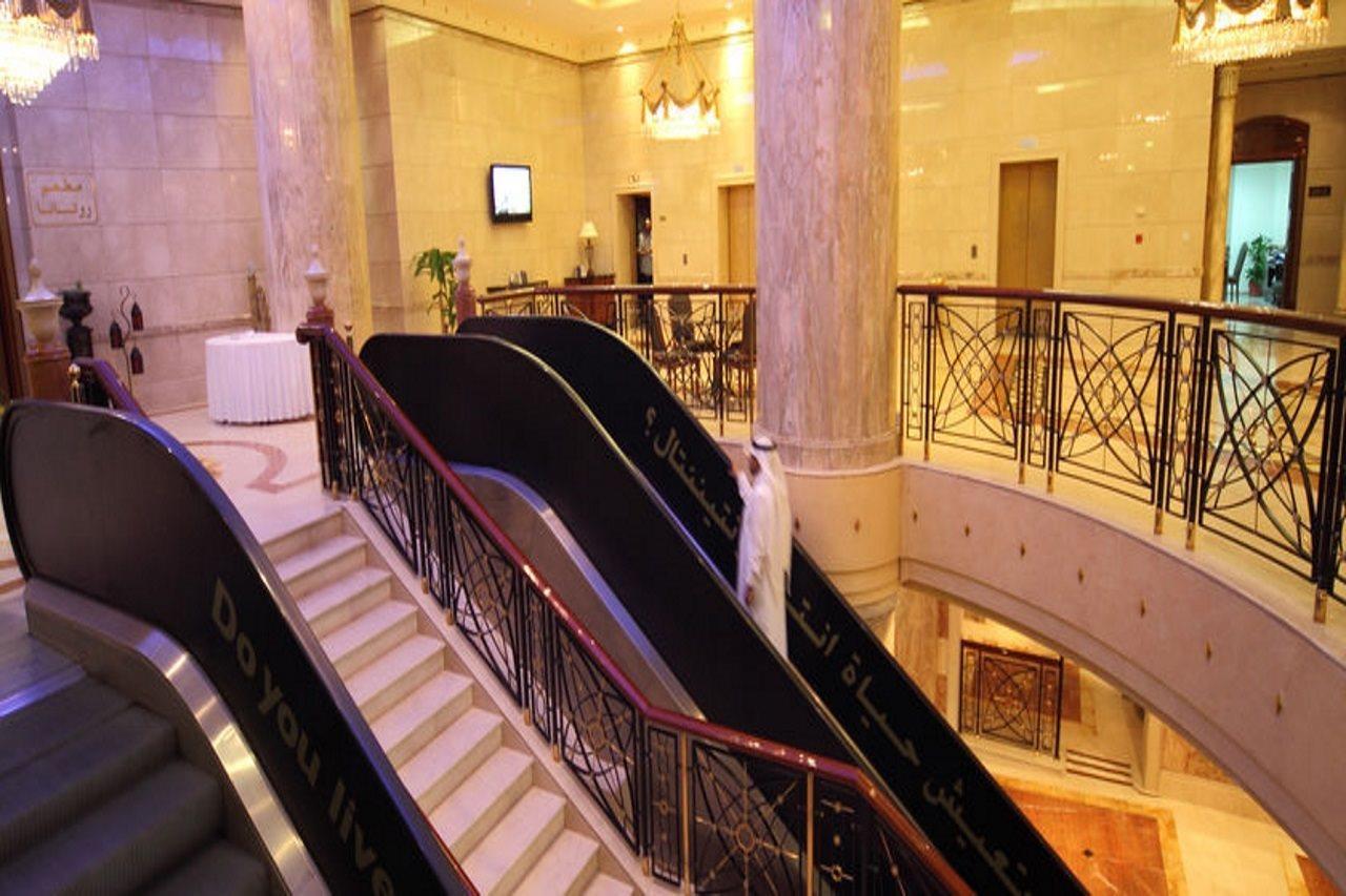 Intercontinental Dar Al Iman Madinah By Ihg Medina Interior foto The photo depicts an elegant interior space, likely within a hotel or a large building. There is a grand staircase visible, which features a combination of stairs and escalators. The design includes decorative railings and marble pillars, contributin